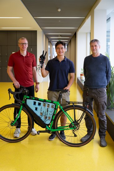 Gruppenfoto, Martin Meister hat in der rechten Hand einen Handschuh und vor ihm steht ein Fahrrad aus dem Bikelab mit Messtechnik