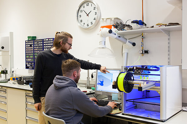 Exohand Zwei Studenten vor einem 3D-Drucker.