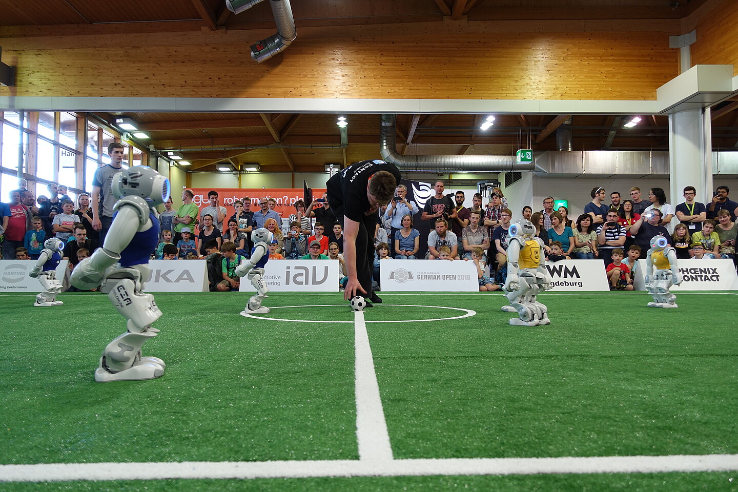 Anstoß im Finale: das Nao-Team HTWK (in blau) gegen die Nao Devils aus Dortmund. (Foto: Nao-Team HTWK). humanoide Fußballroboter auf dem Feld, Anstoßß durch Schiedsrichter