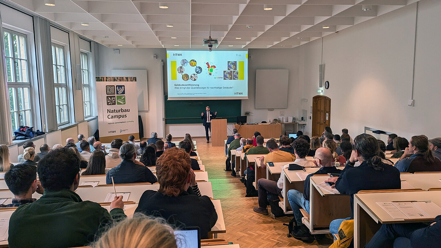 Vortrag Nachhaltig Bauen und Sanieren Menschen sitzen im Hörsaal und vorne spricht ein Redner.