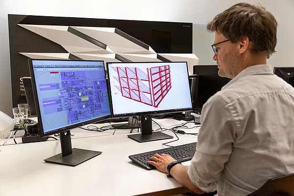 Algorithmen Stefan Huth sitzt am Schreibtisch vor zwei großen Bildschirmen, die Algorithmen zeigen