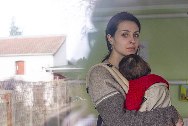 Safe Space eine Frau trägt ein Baby in der Trage und schaut in die Kamera