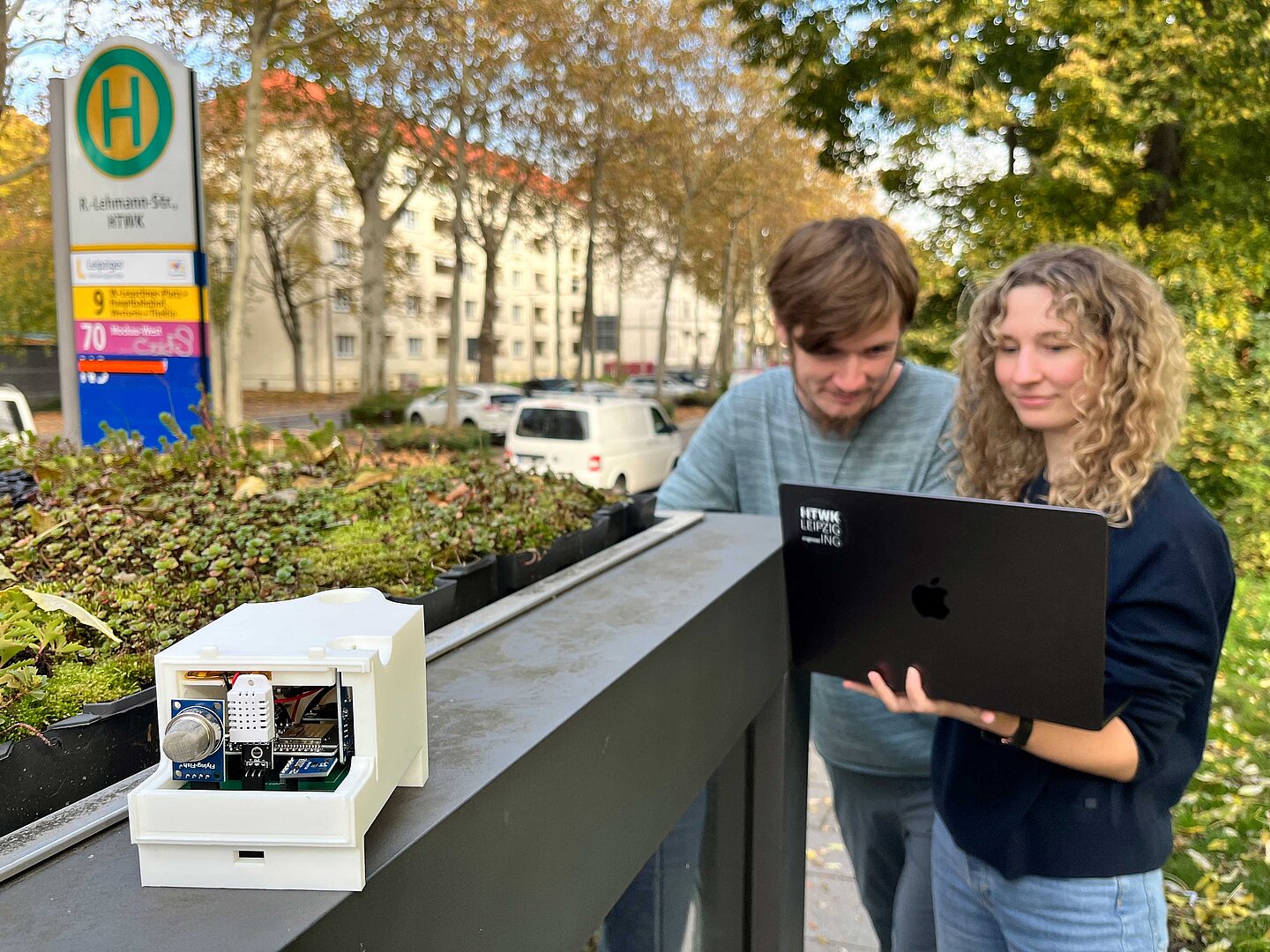 Die wissenschaftliche Mitarbeiterin Stefanie Penzel und die studentische Hilfskraft Philipp Lorenz an einer Haltestelle mit einem Messgerät