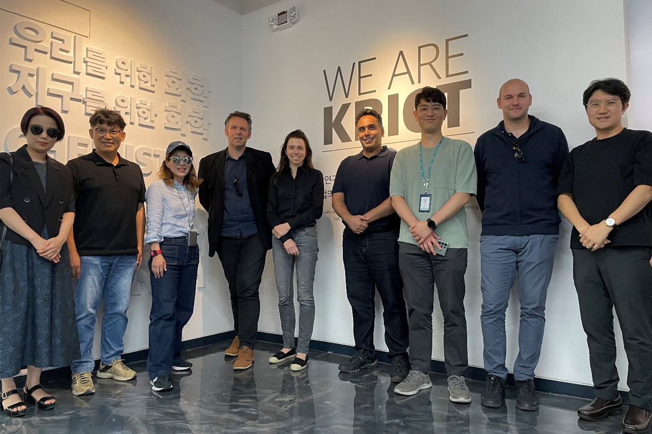 Gruppenfoto von Prof. Böhm und seinem Team mit Wissenschaftlerinnen und Wissenschaftlern, alle lächeln in die Kamera, Innenaufnahme, Logo des KRICT im Hintergrund