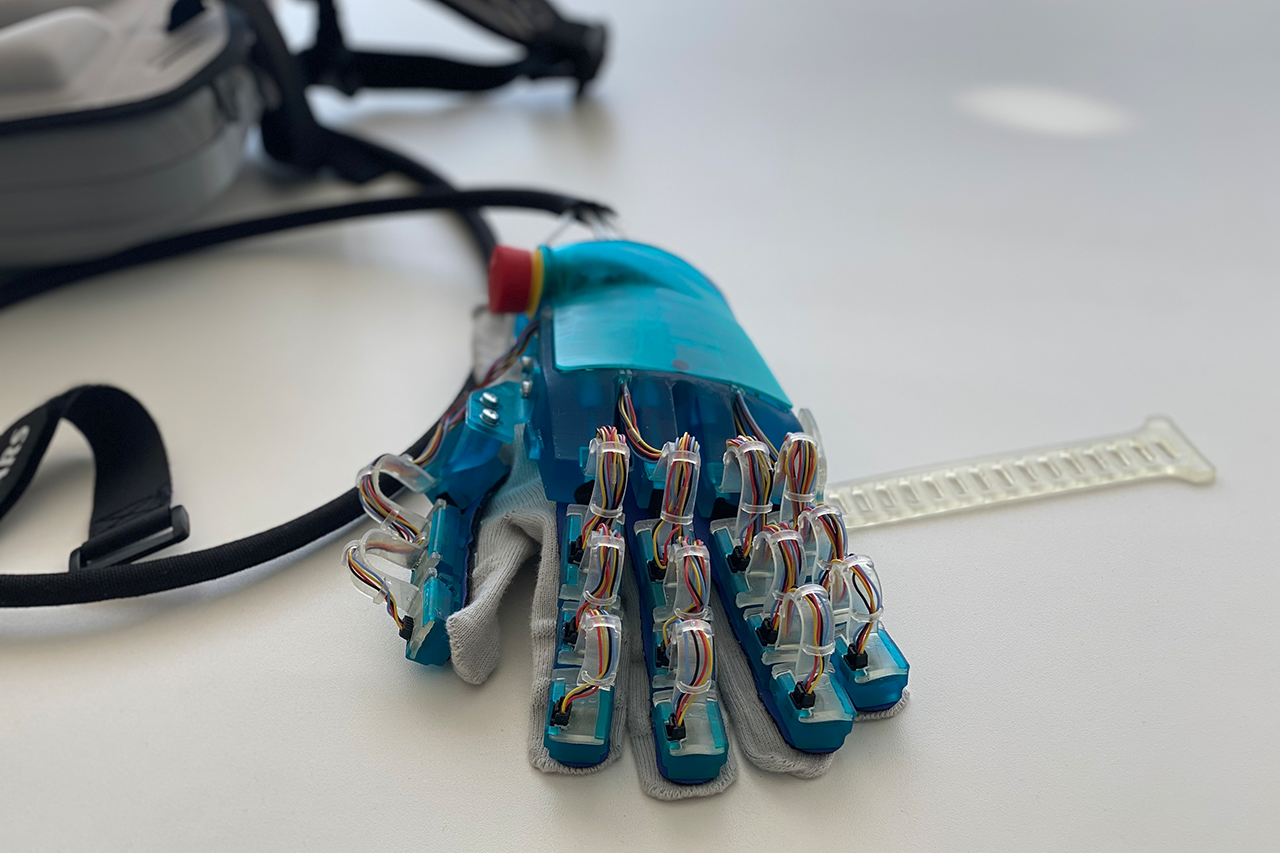 Prototyp einer Exohand, blauer Handschuh mit Kabeln/Verlinkung führt zur Projektwebsite